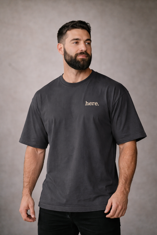 Man wearing subtle union a faded black t-shirt with 'here' text on a gray background